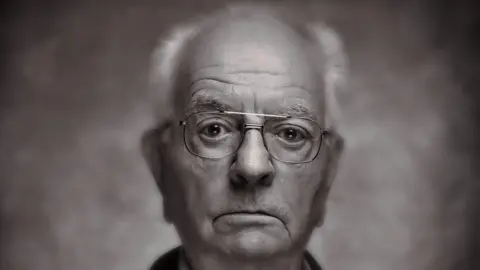 Artistan Photography Cliff Harvey, looking straight at the camera, with glasses on, he has short grey hair. 