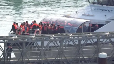 PA Media Migrants wearing red life jackets being brought ashore at Dover by the UK Border Force cutter on 18 October 2024.