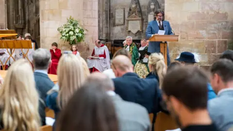 Pictoria Laurence Llewelyn-Bowen wears a blue suit as he gives a reading to the audience at Gloucester Cathedral.