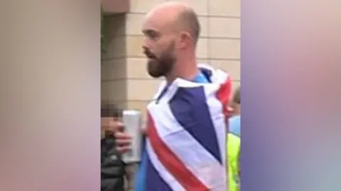 Crown Prosecution Service Kieran Usher holding a can and wearing a union jack flag around his shoulders.