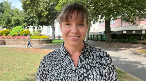 Fiona Vacher standing in a park-like area with trees, flower beds and pathways in the background.