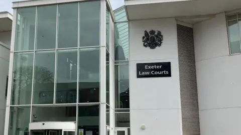 An exterior view of Exeter Crown Court. The building is white with large windows and a black sign which says 'Exeter Law Courts' in white writing.