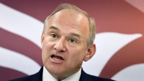 EPA The face of Ed Davey. Behind him is part of a red and white emblem.