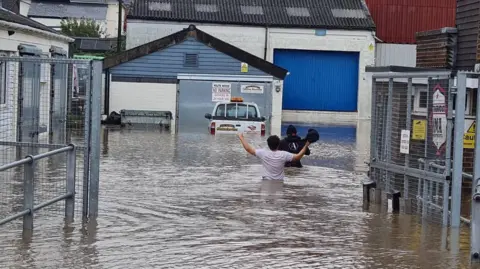 Ken Oatley Two people wade up to their waists in flood water in a street in Ryde on 25 Oct 2023