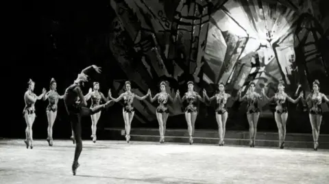 A still from the ballet, showing a line of dancers en pointe