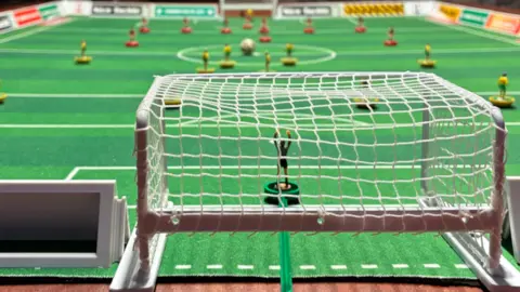 Edd Smith/BBC A close up of a Subbuteo set with miniature goal posts and plastic figurine football players.