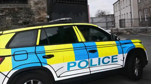 Pacemaker Press Shows a police car in yellow blue and white colours with the word "police" on the side entering a court complex. 