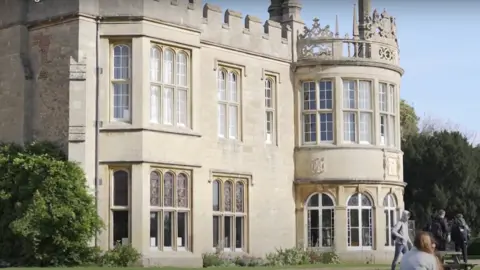 Hinchingbrooke School Part of Hinchingbrooke School shows an ornate, pale stone building with floor-to-ceiling windows and a turret on top of the first floor. A few pupils can be seen in the grounds in front of the building.