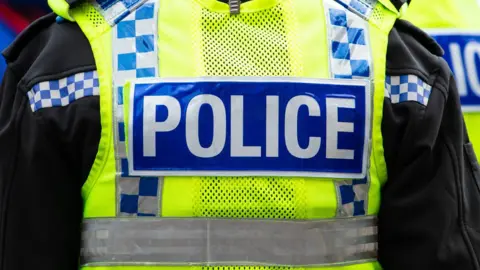 The back of a police officer's yellow high vis vest. It says "Police" in white on a blue strip.