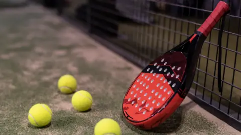 Getty Images A red and black padel racquet near four yellow balls on a green court 