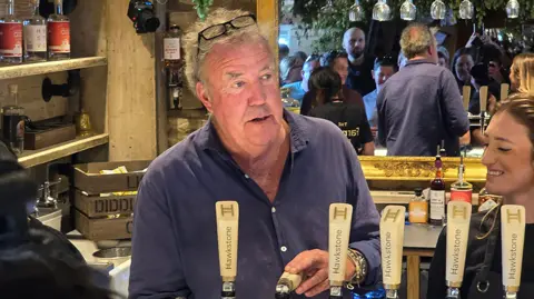 PA Media Jeremy Clarkson inside his pub, in front of a large mirror, pulling a pint