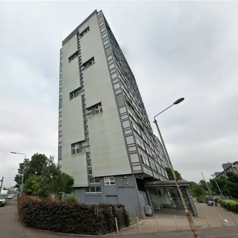 Google Waddell Court, a large grey multi-storey block rises into the sky, with a sign showing number 83 and "Waddell Court" on the side on the bottom floor.