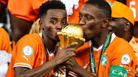 Ivory Coast players Simon Adingra and Max Gradel kiss the Africa Cup of Nations trophy