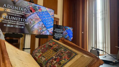 Title page of Great Bible which is colourful with illustrations of the kind in a royal purple robe. Screens are in the background with similar illustrations. 