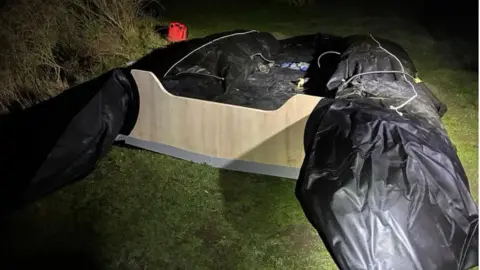 An inflatable boat that was intended for use in a Channel crossing is on an area of grass close to a beach in Belgium.