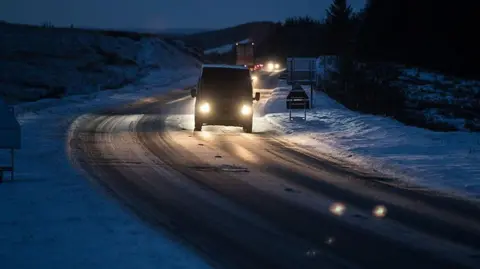 Icy, snowy road in darkness with van driving