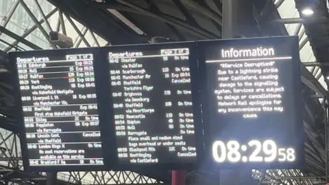 A train station travel board in black with white writing showing a list of departures and information.
