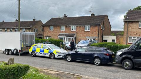 Police officers and a car outside the house in Caddington 