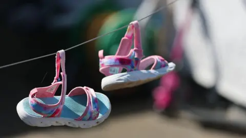 A pair of pink and blue children's sandals hang from a washing line