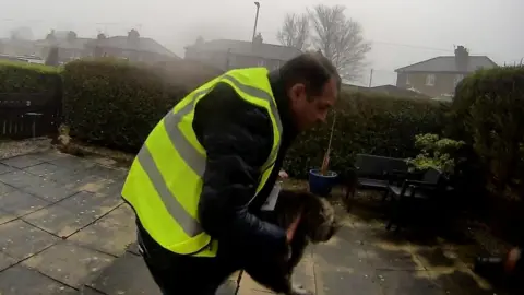 A man in a high vis jacket is seen holding a cat
