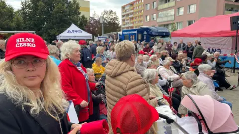 A crowd of people around a group of Sarger, many of whom wear strong red hats in the Czechio/strong red hats including a blonde woman in the foreground. The attendees are greater than the elderly. 