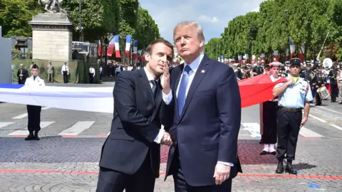 Donald Trump and Emanuel Macron stand in front of a row of French military