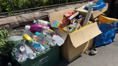 Overflowing boxes of recycling, sitting out on a pavement