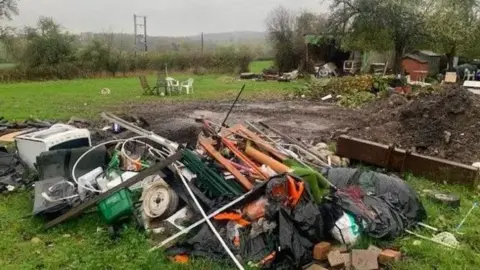 A pile of rubbish can be seen on grass. It's a mixture of bags, plastic and bricks.