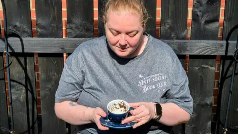 Michelle Liddle Michelle Liddle is sat in front of a wooden fence tilting a blue teacup to show tea leaves inside. She is wearing a grey t-shirt and her blonde hair is tied back.