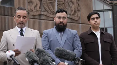 PA Three men in suits outside a court. Microphones are pointed towards them.