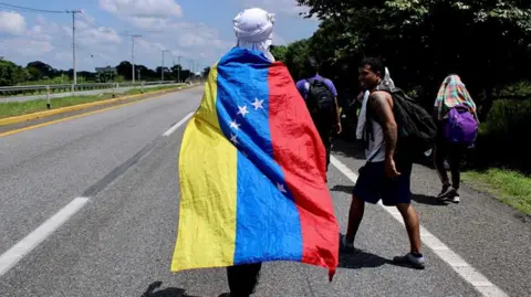 Reuters A migrant holds a Venezuelan flag while walking with other migrants as they participate in a caravan after growing impatience waiting for a humanitarian visa to cross the country and reach the U.S. border, in Cerro Gordo in Huixtla near Tapachula, Mexico July 1, 2022. 