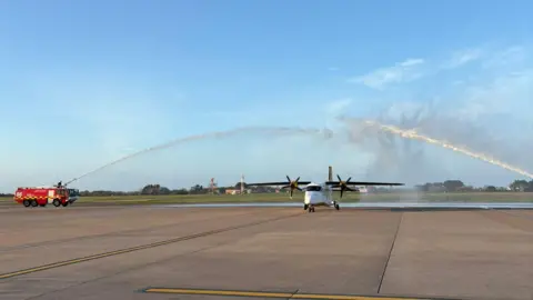 A picture of a plane making its final landing. It is being sprayed with water. 