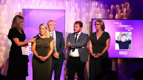 Four members of the In Charley's Memory team accepting their award on stage while a pink hue lights up the backdrop. 