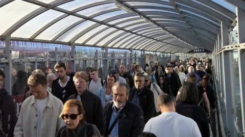 PA Media A lonq queue of people in a roofed tunnel at an airport