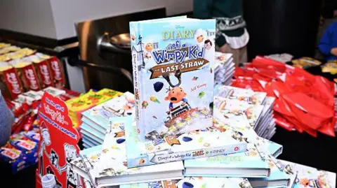 Getty Images Diary of a Wimpy Kid books are seen on sale in a bookshop. The books are stacked up on a table and one is upright on the top of the heap.