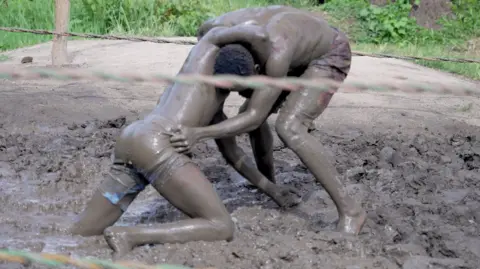 Two men covered in mud wrestle in a ring