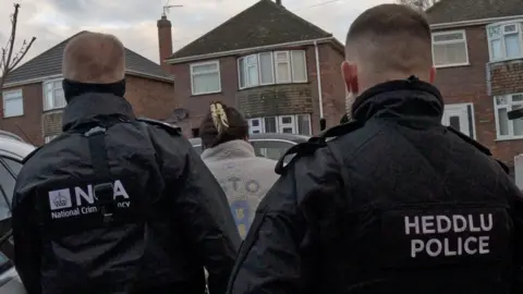 Two National Crime Agency officers arresting a woman in a residental area.