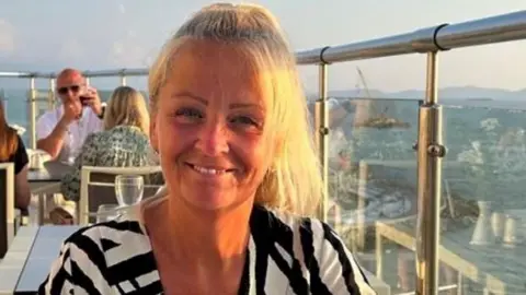 Anita Rose sitting at a table at a rooftop restaurant. She is smiling, has most of her blonde hair tied back and is wearing a black and white striped shirt/top