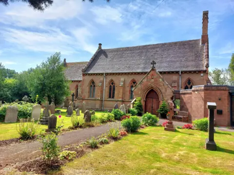 BBC Weather Watchers/Lynn A church in salmon-coloured stone with arched windows and gravestones and flowers in the foreground