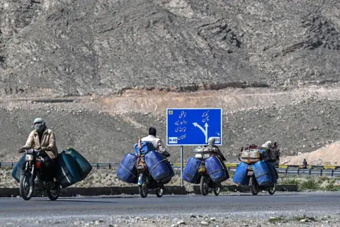 AFP via Getty Images This photograph taken on March 14, 2026 shows vendors transporting jerrycans filled with smuggled Iranian petrol on their motorcycles, on the outskirts of Quetta in Balochistan province. (Photo by Banaras KHAN / AFP via Getty Images)