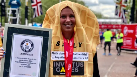 Sally Orange A woman dressed as a nut and standing after the finish at the London Marathon smiles as she holds up a framed Guinness World Record certificate.