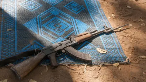 A rifle rests on top of a prayer mat.