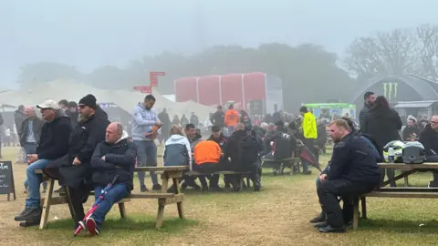 Fans sitting on picnic benches in the fan park, which is a grassed area with marquees and food trucks around the edge.