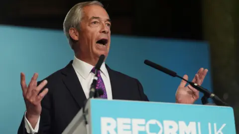PA Media Nigel Farage in a black suit and purple tie stands in front of a podium with "Reform UK" written on it, with its turquoise-coloured branding.