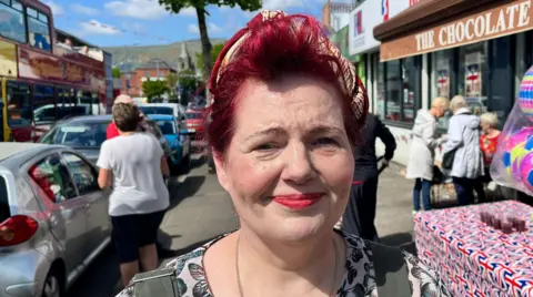 A woman with red hair, tied up, smiling at the camera. She is standing on a busy street. 