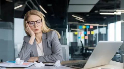 Getty Images Tired and disappointed businesswoman sitting near documents and scraps of paper.