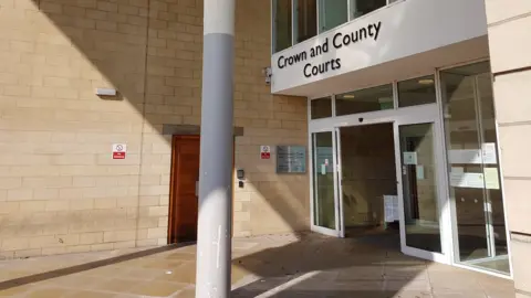 A courtyard before the entrance of Northampton Crown Court, with a sign reading "Crown and County Courts" above glass doors