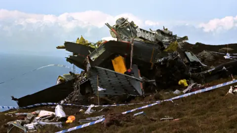 wreckage of an aircraft on a hillside surrounded by police tape