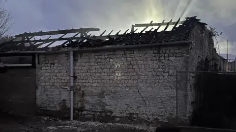 A stone barn with the burnt out embers of a wooden roof on display. 