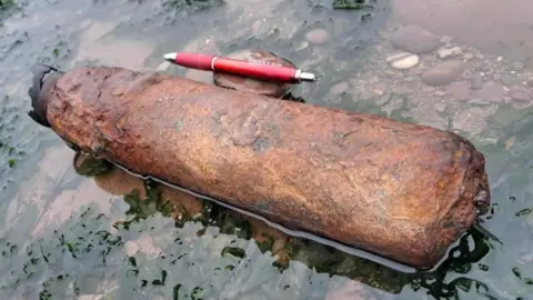 A rusted wartime artillery item that was found on the Watchet coastline with a pen next to it for size comparison